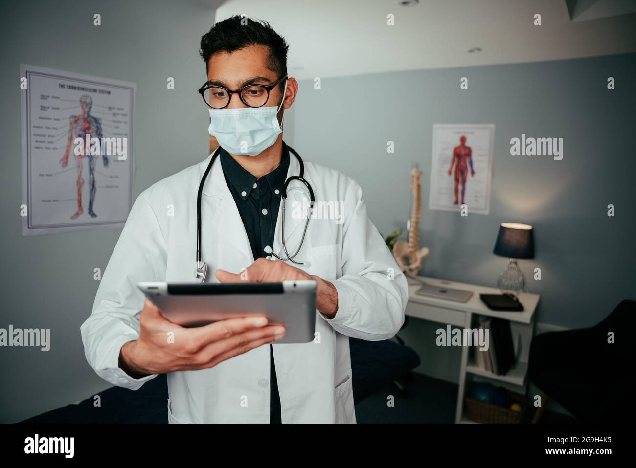 Mixed race male doctor working from office typing on digital tablet Stock Photo