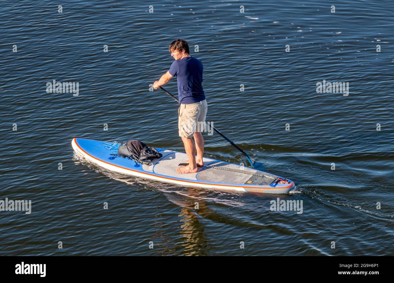 a man on a stand-up paddle board on the sea paddling wearing shorts and keeping balance. Stock Photo