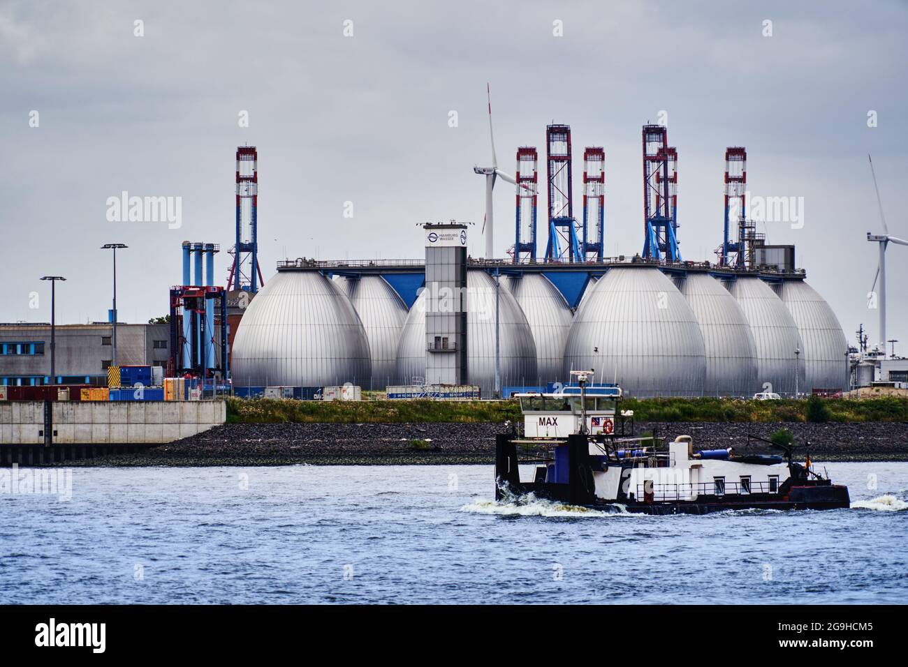 Hamburg, Germany, July 22, 2021: Digesters of a sewage treatment plant of the Hamburg waterworks on the Elbe with a ferry in the foreground on the riv Stock Photo