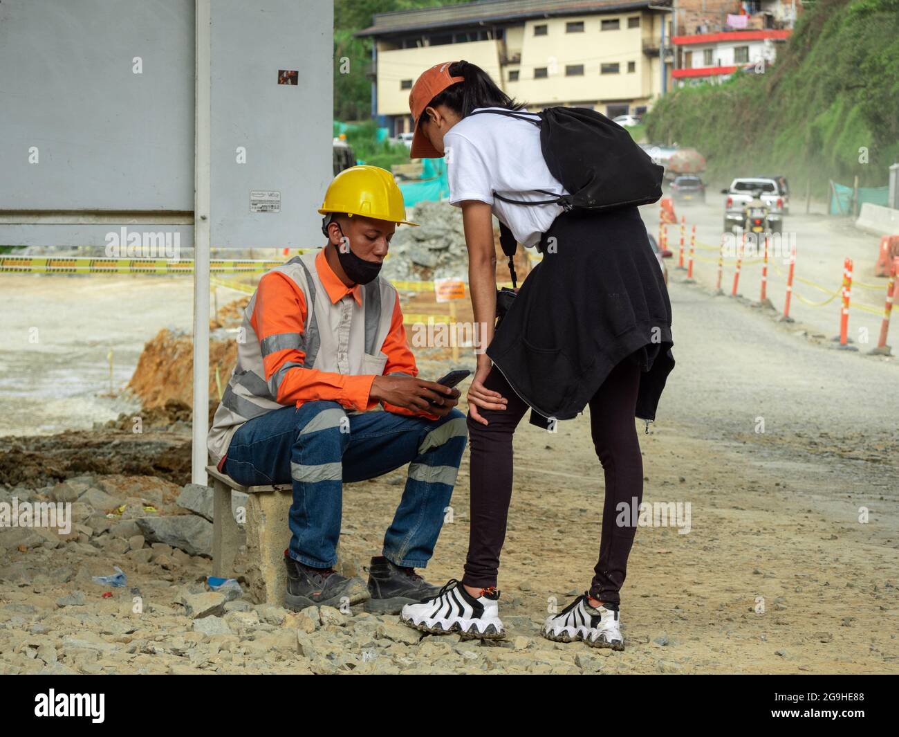 Amaga, Antioquia, Colombia - July 18 2021: Young Latin Woman in Sportswear Asks for the Phone Number of a Man Wearing a Black Mask, Yellow Hard Hat an Stock Photo