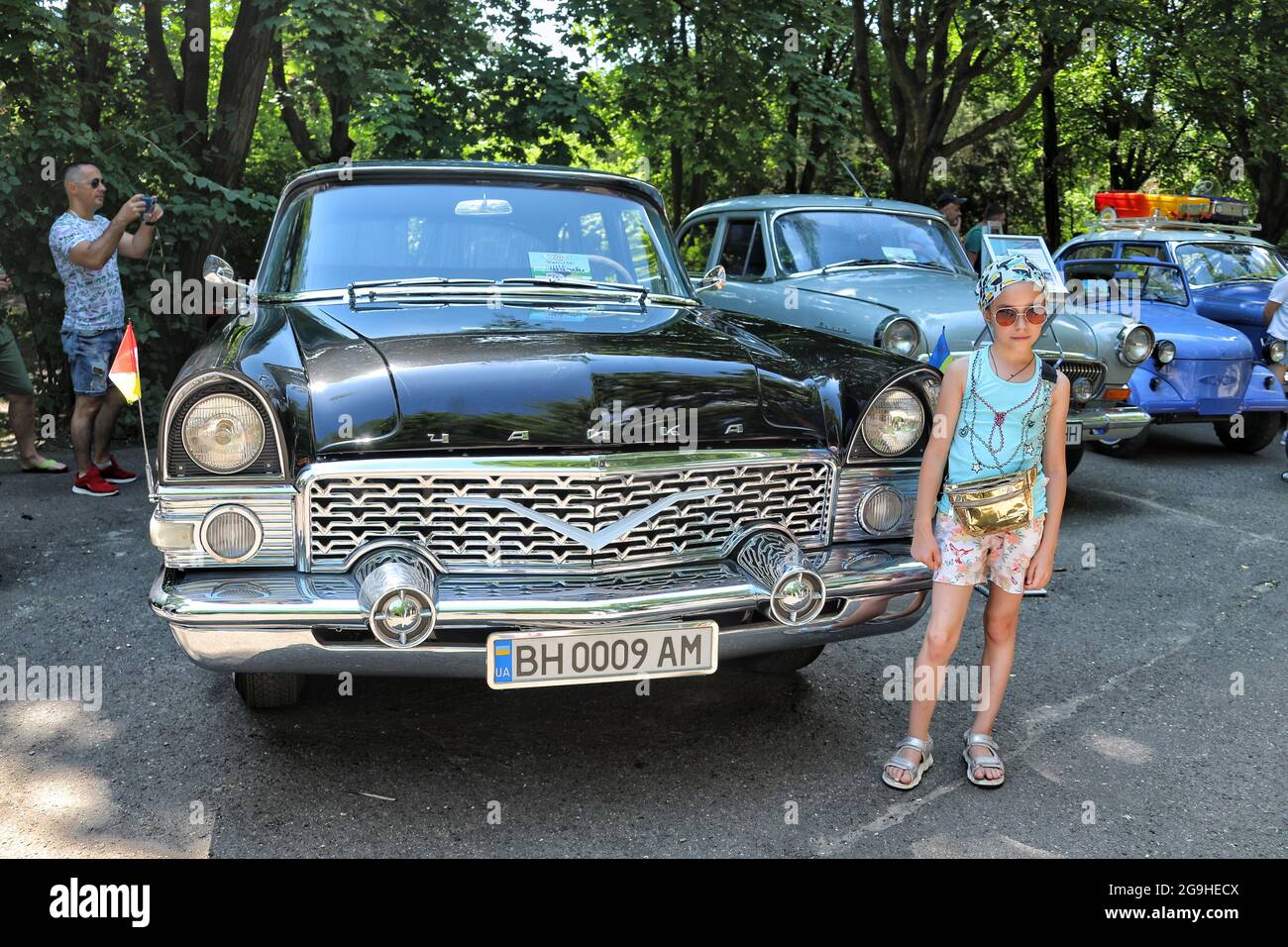 ODESA, UKRAINE - JULY 24, 2021 - A girl poses for a photo next to a black GAZ Chaika during the Old School Weekend 2021 car show in Odesa, southern Uk Stock Photo