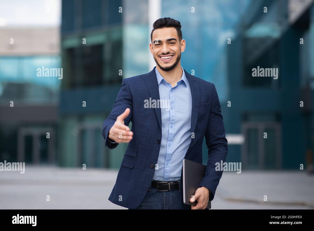 https://c8.alamy.com/comp/2G9HFEX/positive-millennial-arab-man-in-formal-stylish-suit-outstretching-hand-towards-camera-and-smiling-greeting-business-partner-next-to-office-building-2G9HFEX.jpg