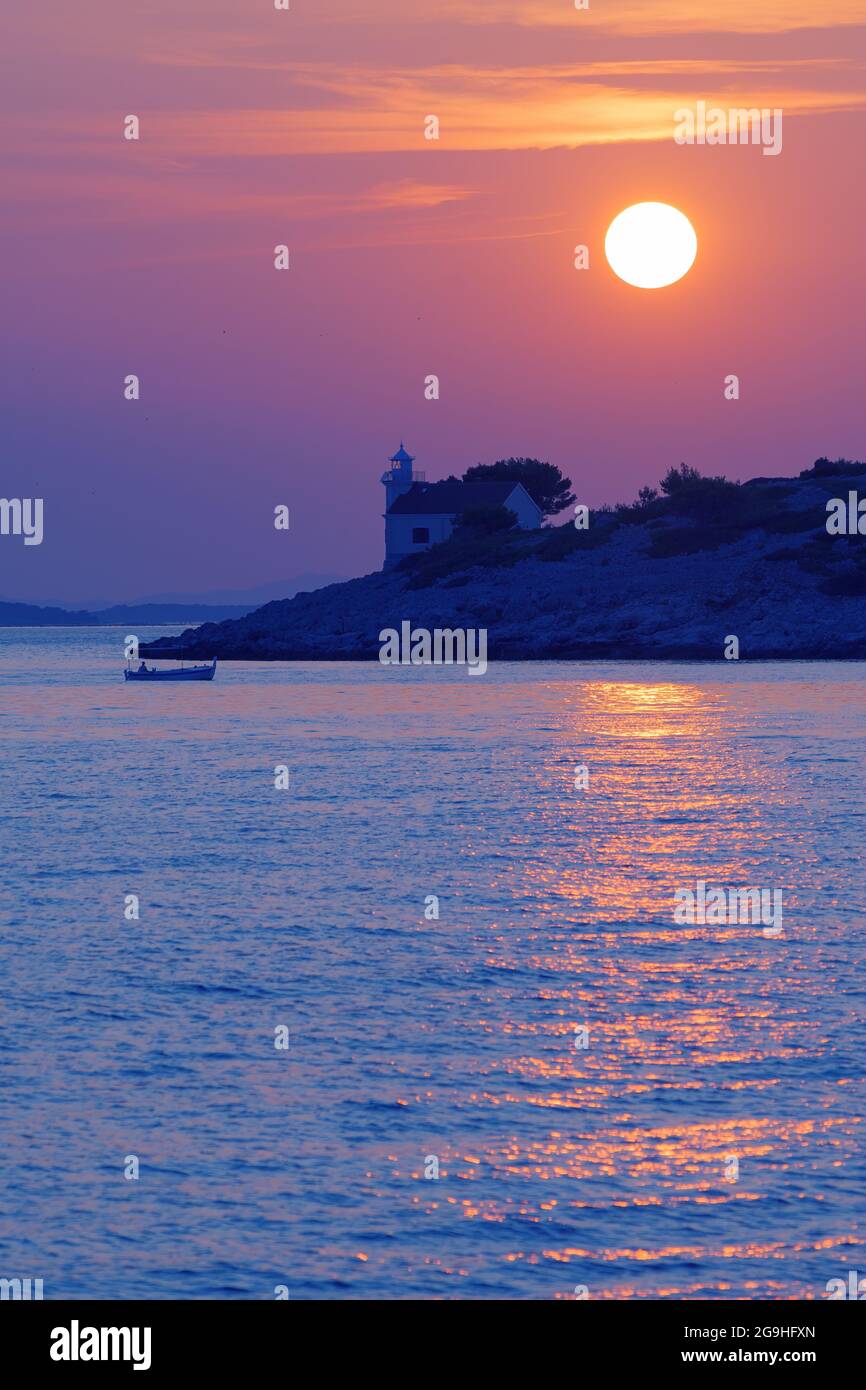 Beautiful sunset over desolate lighthouse on Croatian island Murter in Adriatic sea and fisherman in a boat. Holidays, travel, tourism, summer and pea Stock Photo