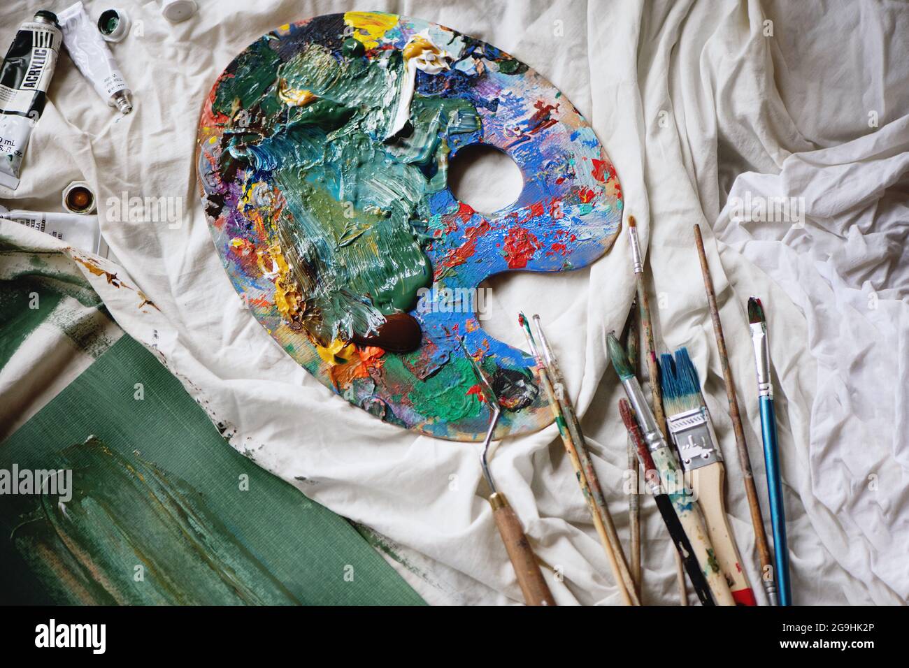 Artist paint brushes and palette on white cloth background. Stock Photo