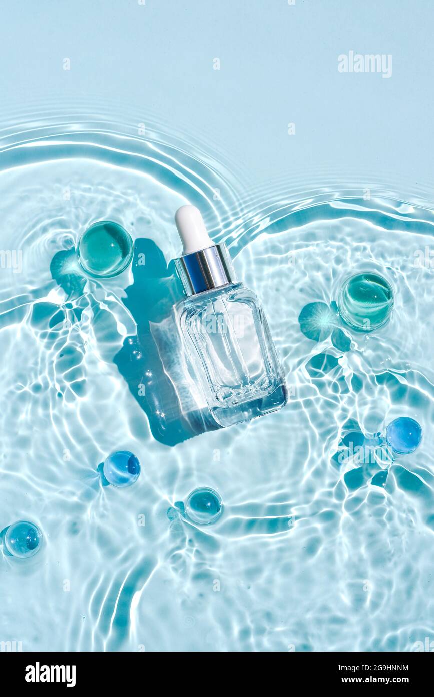 Mockup of cosmetic glass blue bottle with pipette and serum on water surface with waves. Advertising of a medical product for anti-aging care, moistur Stock Photo