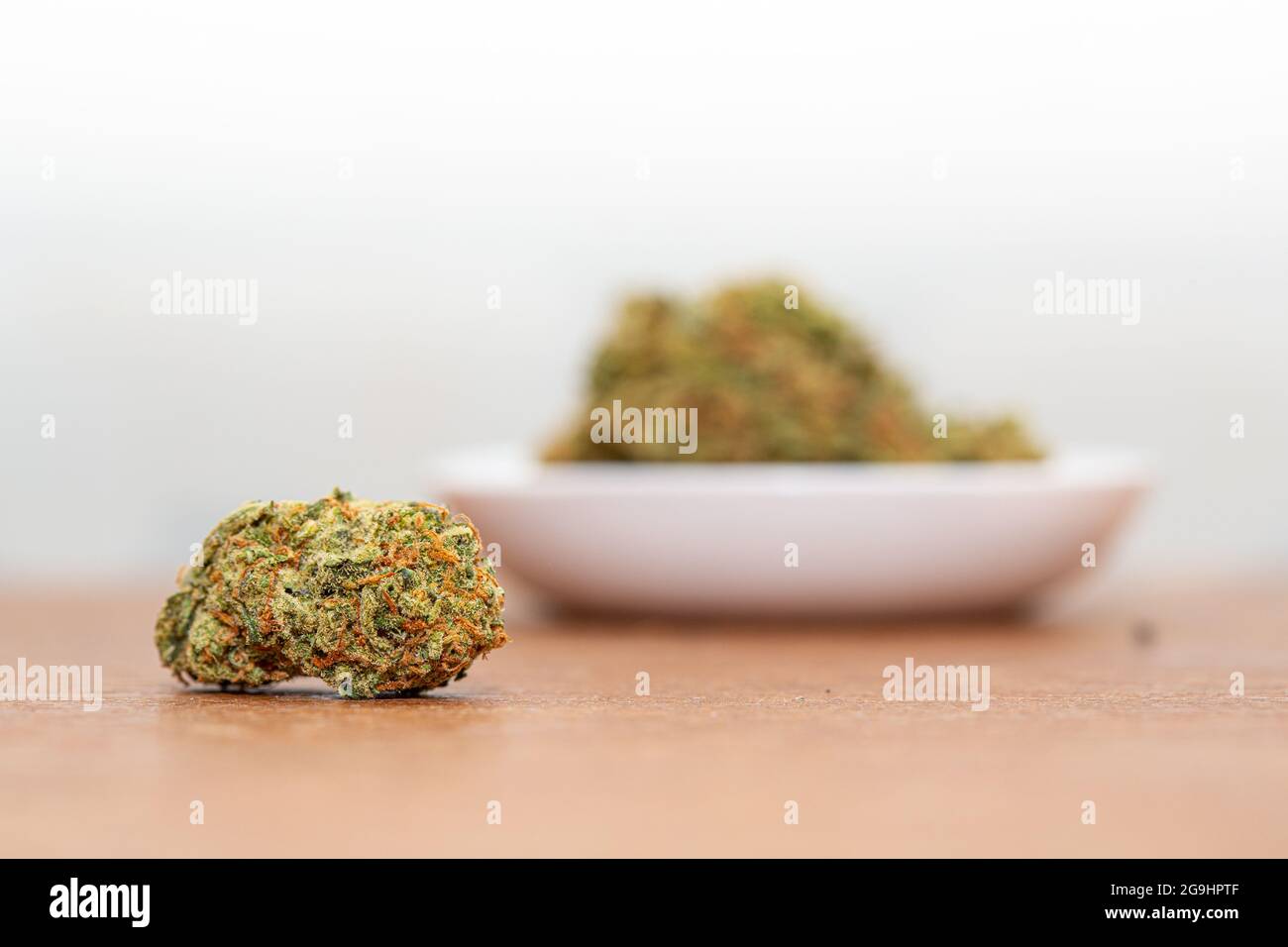 A small cannabis bud on a table with a blurry bowl in the background. Stock Photo