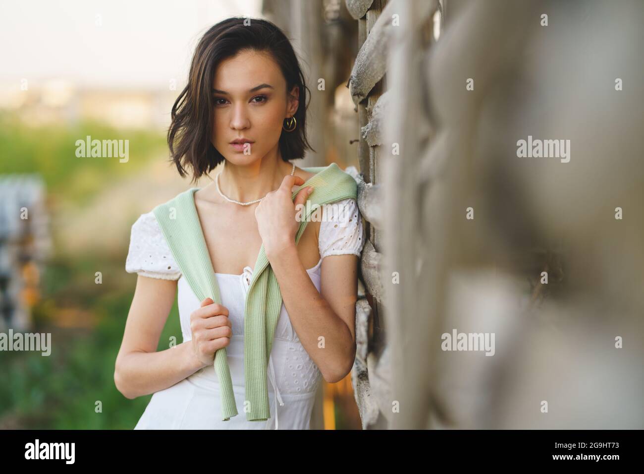 Asian woman, posing near a tobacco drying shed, wearing a white dress and green wellies. Stock Photo