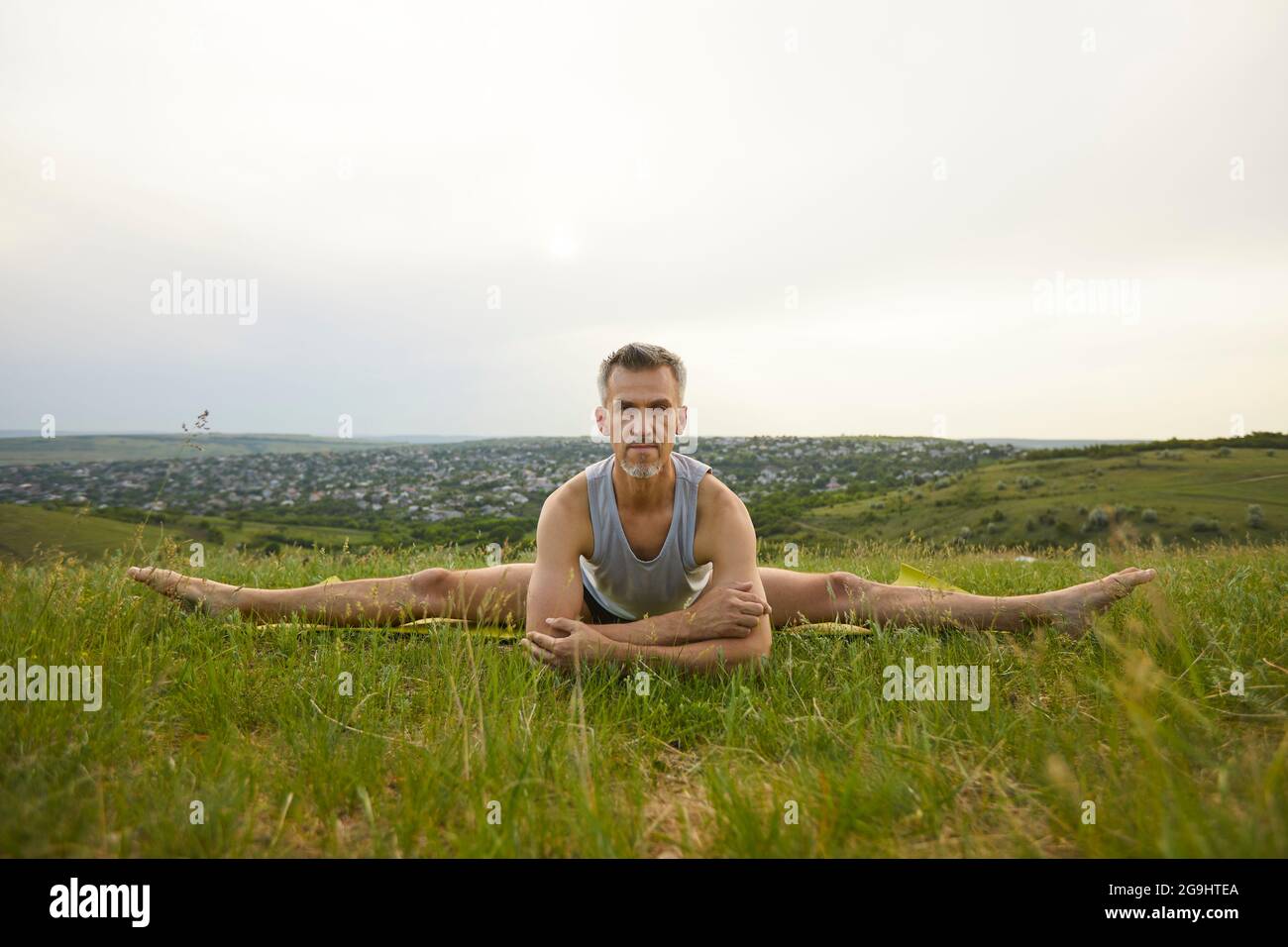 Serious male yoga instructor practicing stretching leg exercise in green summer meadow Stock Photo