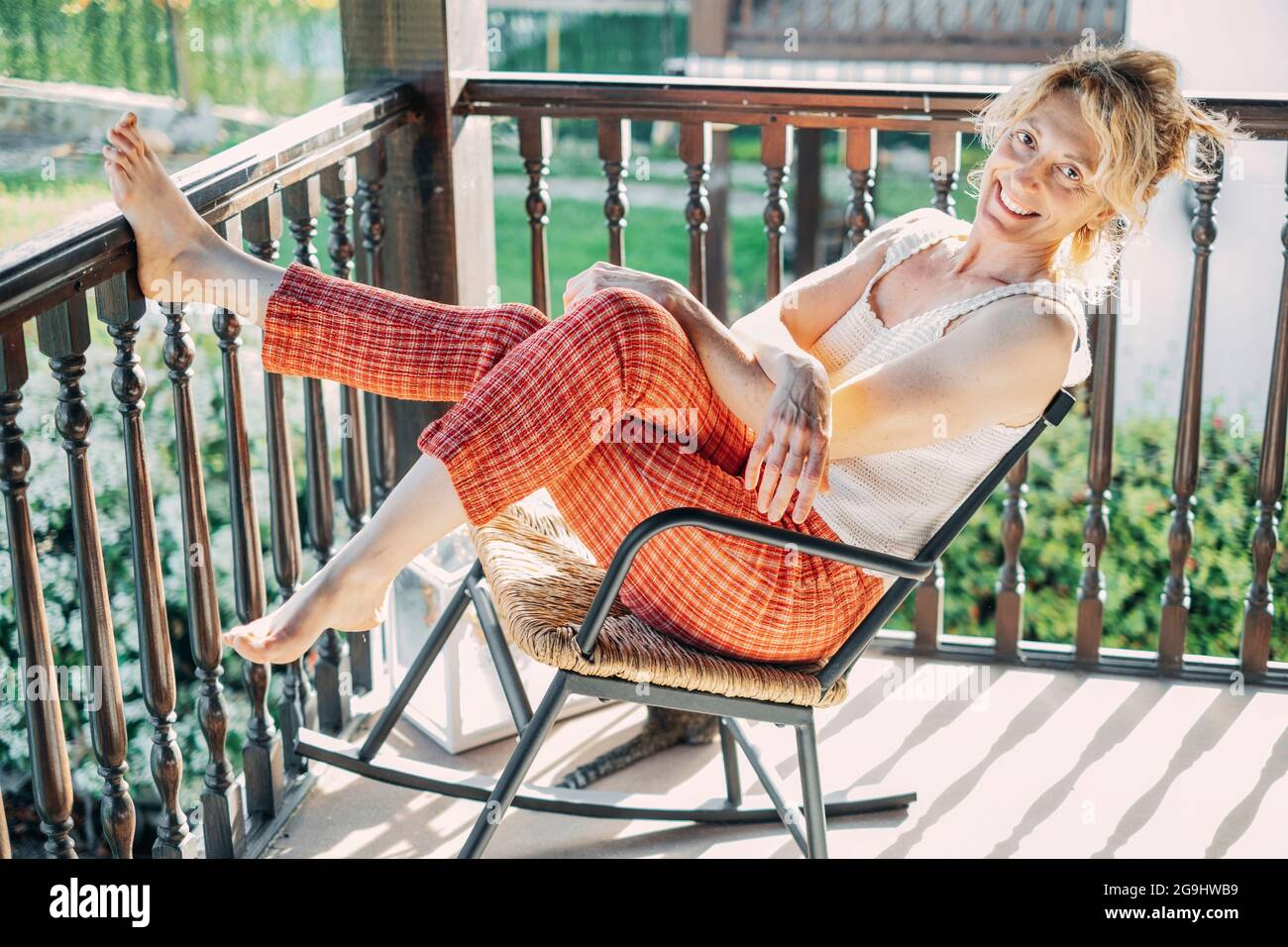 portrait of a young mature caucasian blonde woman relaxing at home on the porch sitting in a rocking chair. Lifestyle concept. Stock Photo
