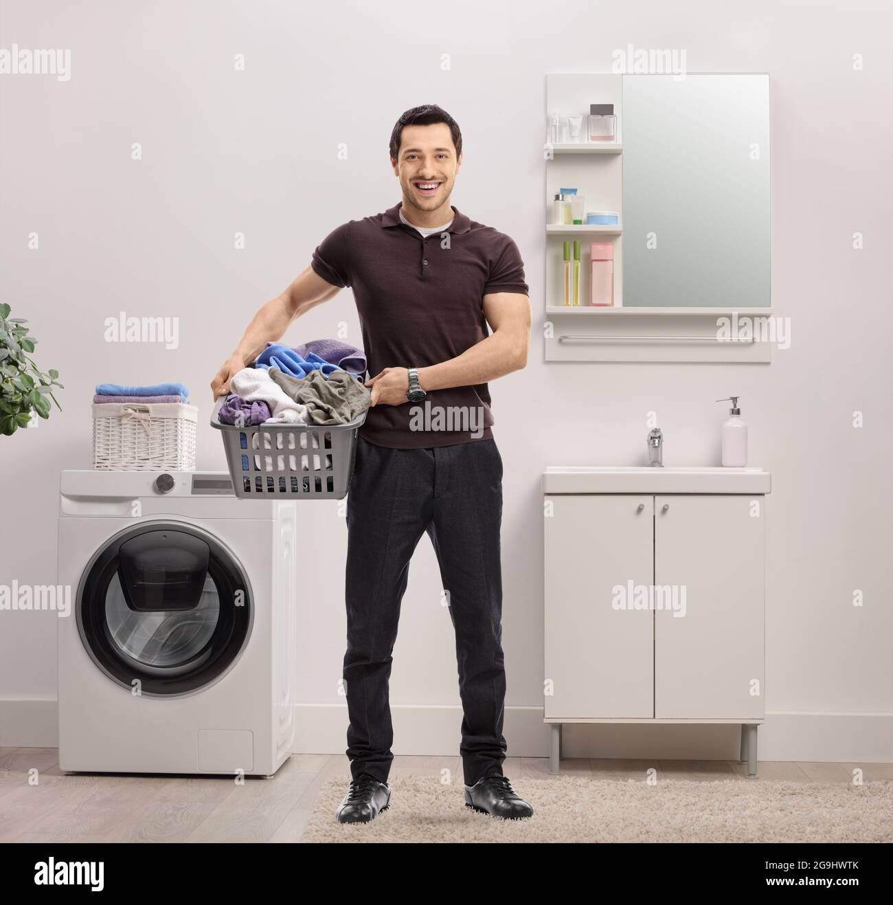 Young man with a laundry basket full of clothes standing in a bathroom Stock Photo