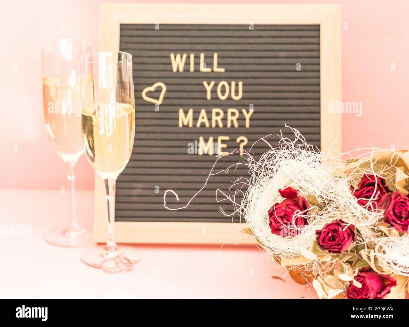https://c8.alamy.com/comp/2G9J0WX/glasses-of-champagne-a-bouquet-of-artificial-flowers-and-will-you-marry-me-board-on-the-table-2G9J0WX.jpg
