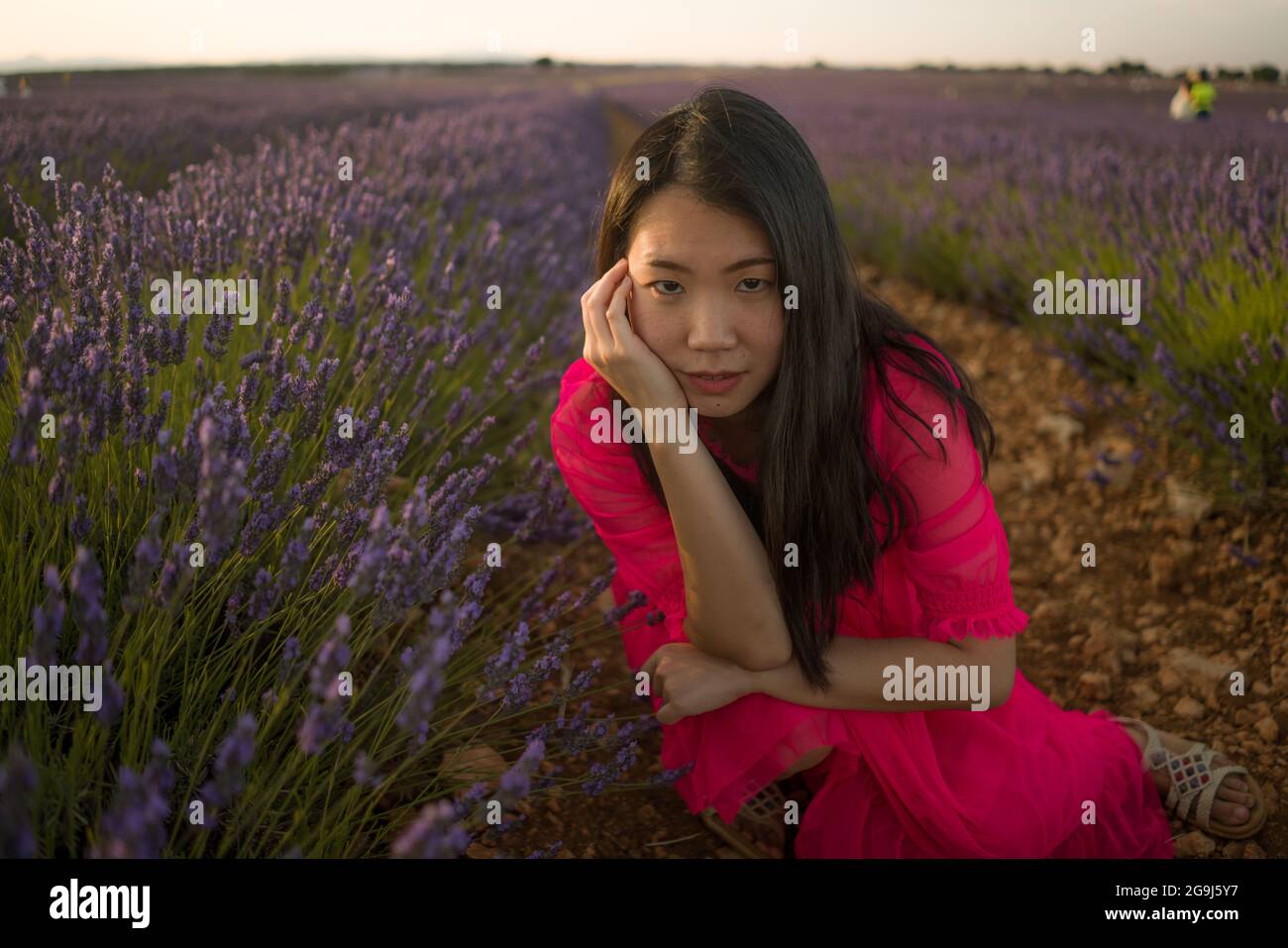 young Asian woman outdoors at lavender flowers field - happy and beautiful Japanese girl in sweet Summer magenta dress enjoying holidays relaxed on pu Stock Photo