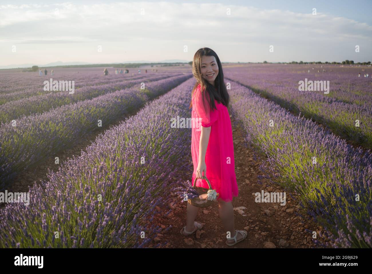young Asian woman outdoors at lavender flowers field - happy and beautiful Korean girl in sweet Summer magenta dress enjoying holidays relaxed on purp Stock Photo