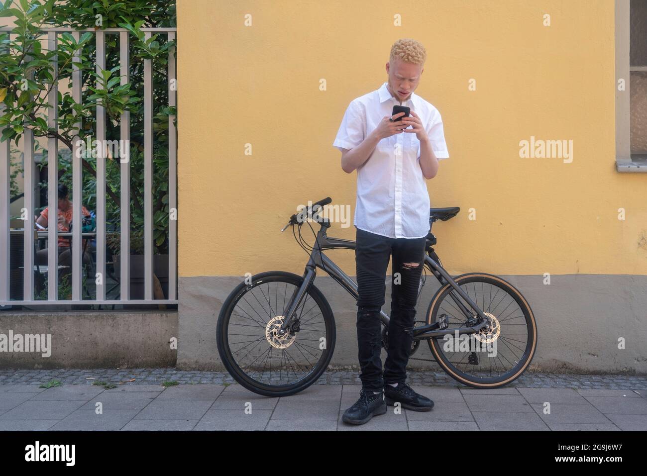 Germany, Cologne, Albino man using smart phone in front of building and bicycle Stock Photo