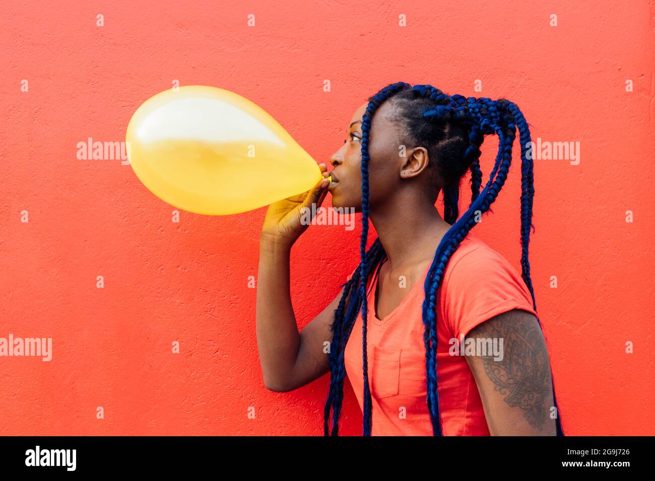 Italy, Milan, Young woman with braids blowing yellow balloon Stock Photo
