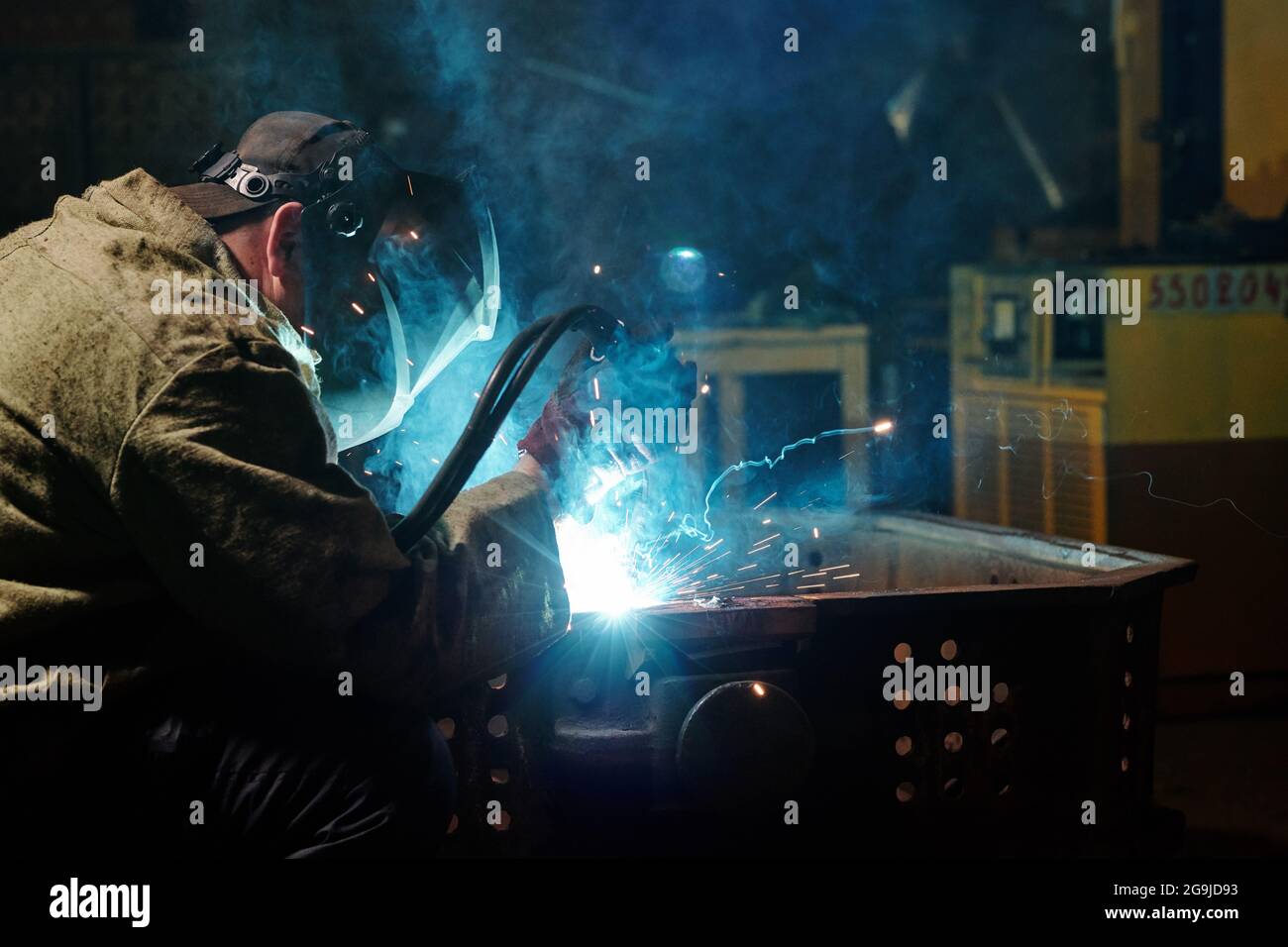 Worker in protective mask using angle grinder in workshop Stock Photo