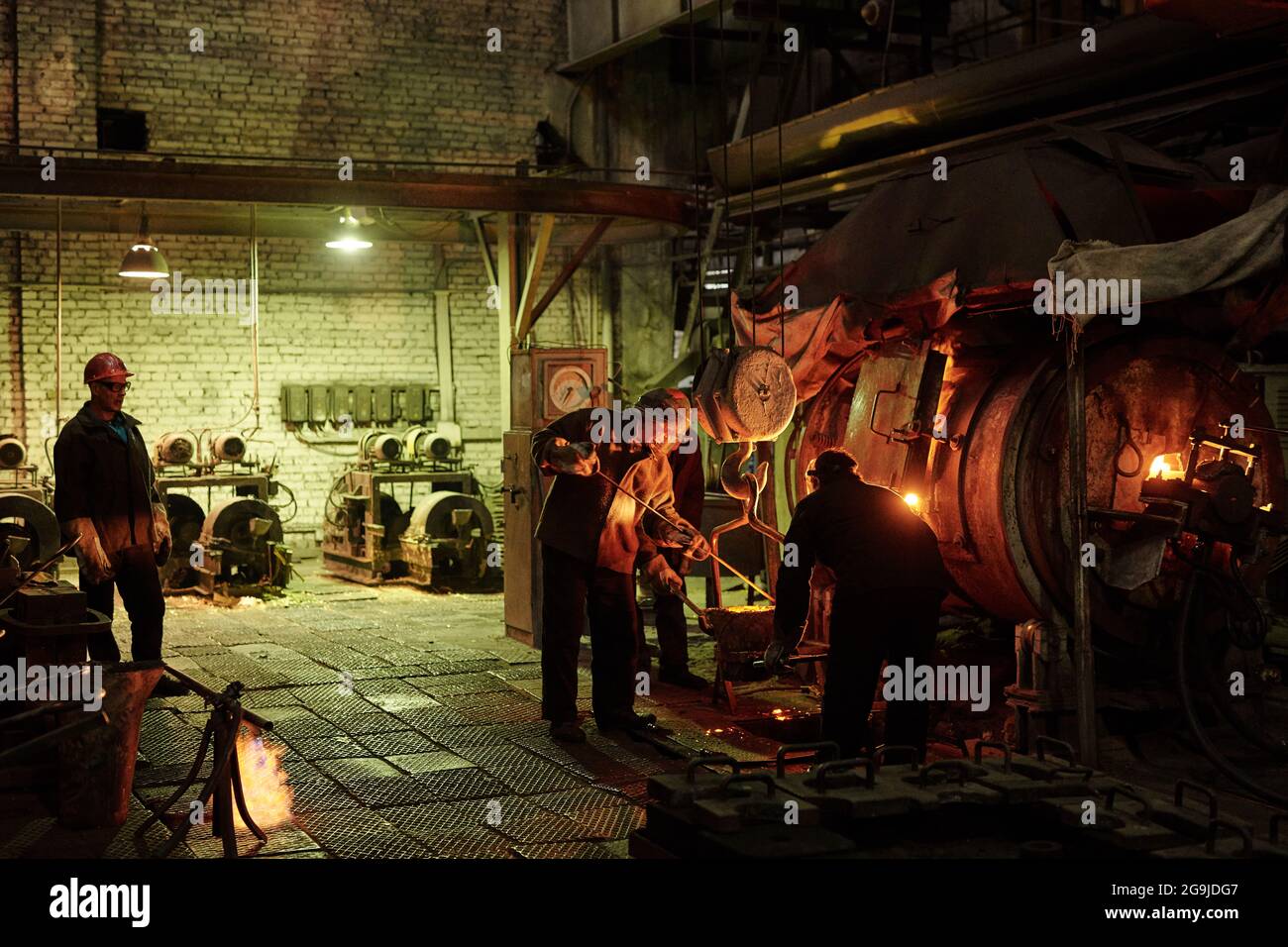 Workers in helmets working in team they melting iron in metal factory Stock Photo
