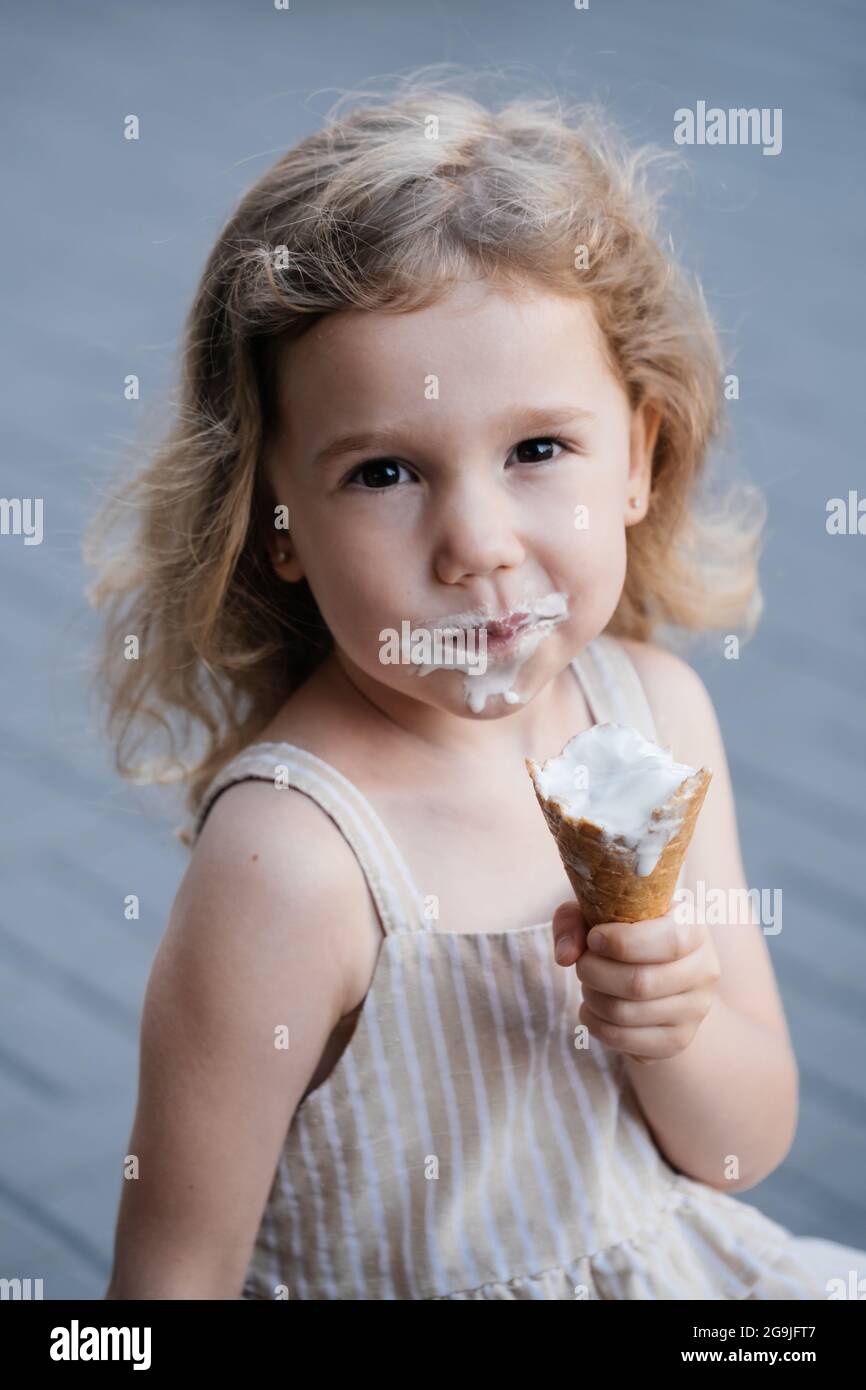Toddler child eating cone ice cream outside near cafe. Cute blonde