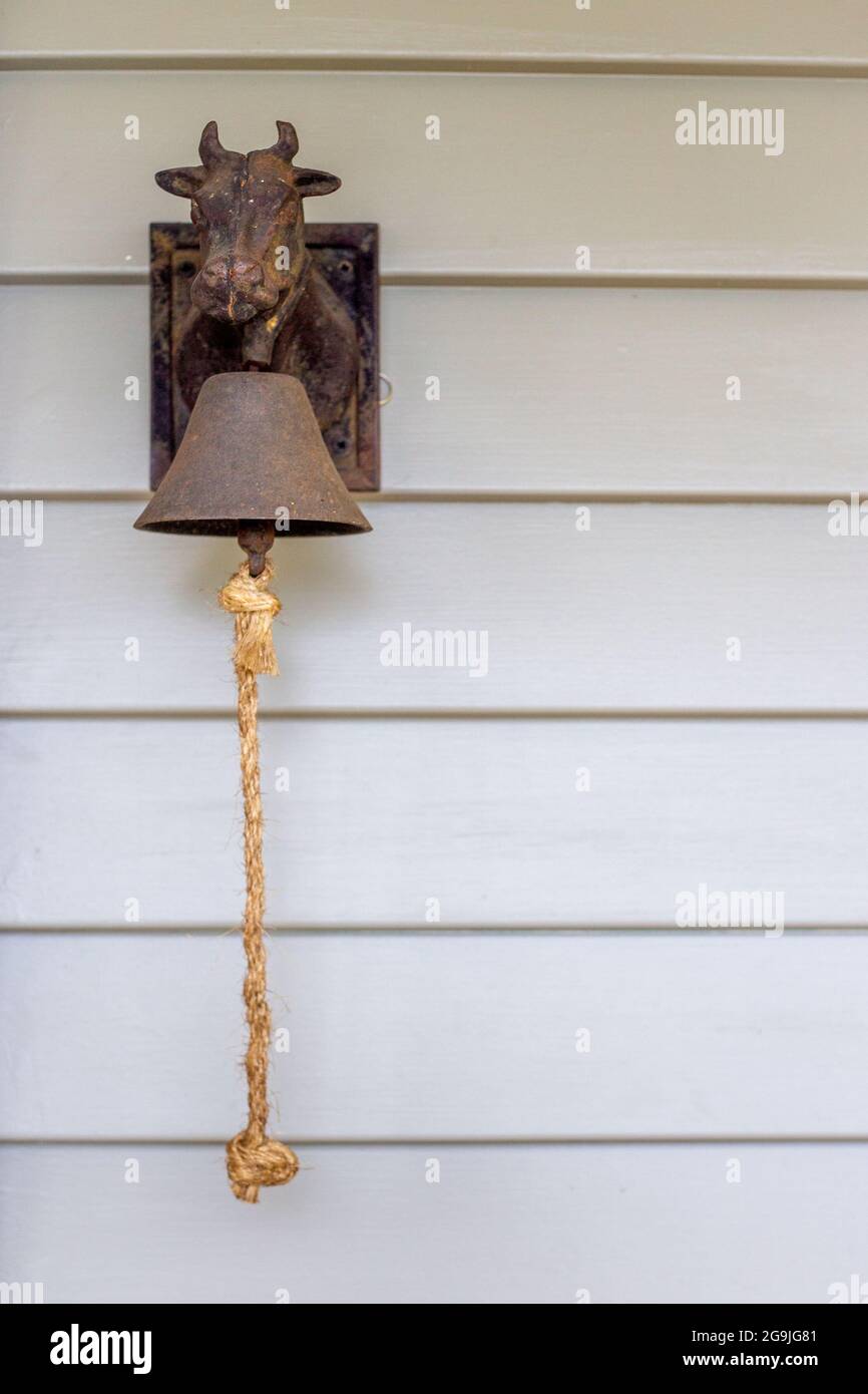 A cast iron cow door bell hangs on a rural weatherboard cottage at the back door to summon the family for meals, phone calls etc Stock Photo