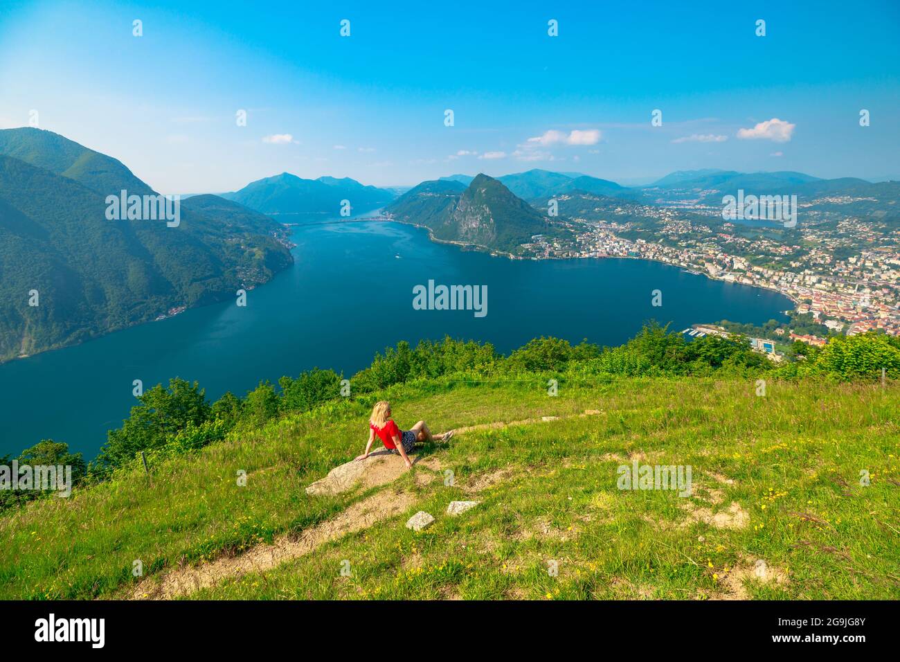 Woman sitting on top of Lugano Swiss city by Lugano Lake in Switzerland. Aerial view lookout from Monte Bre Mount. Lugano cityscape with San Salvatore Stock Photo