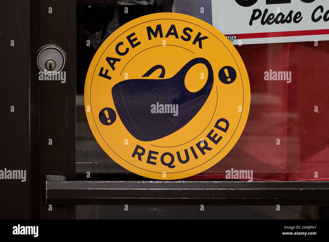 Strathroy, Ontario, Canada - June 28 2021: A face mask required sticker, wet from the rain, on the front glass door of a storefront. Stock Photo