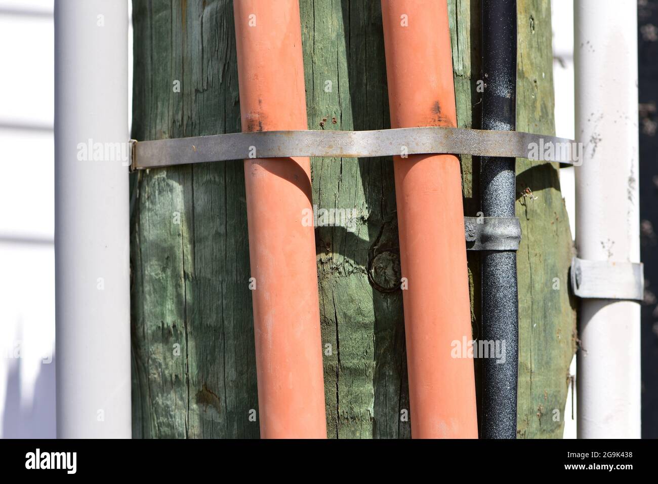 Detail of electric grid pole with cables in plastic tubes held by metal clamps. Stock Photo