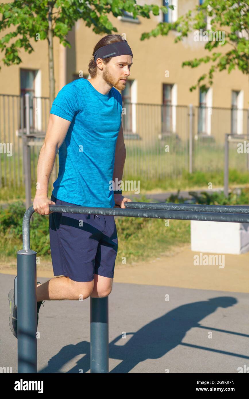 Young athletic man pulling up on parallel metal bars while working out on stadium Stock Photo