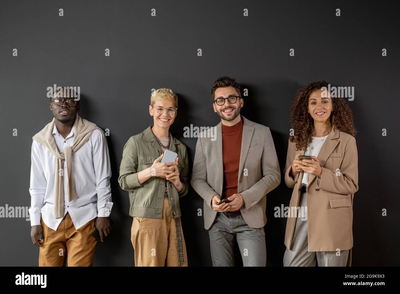 Young successful people with smartphones standing against grey wall Stock Photo
