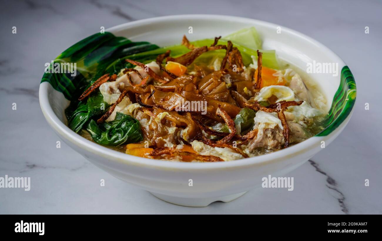 Flat Noodles cooked in Egg Gravy (Wan Tan Hor) with chicken bits and fish balls. Garnished with fried onions. A chinese cuisine served in Southeast As Stock Photo