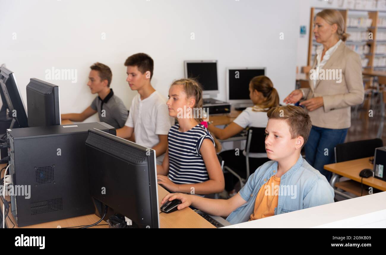 Schoolchildren using computers and teacher teaching them Stock Photo ...