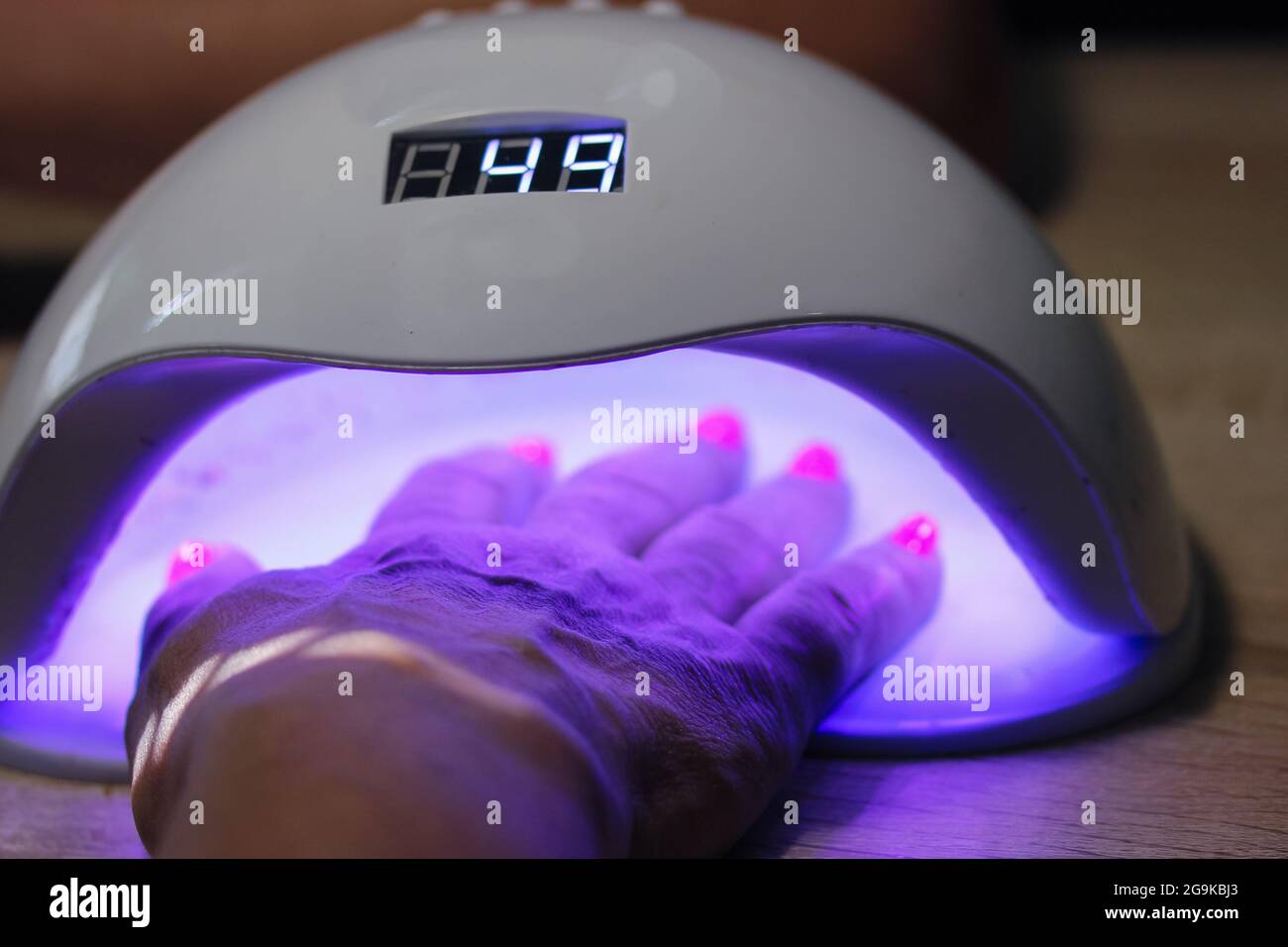 Woman hand inside UV LED lamp for drying pink nails with gel method, plate curing close up