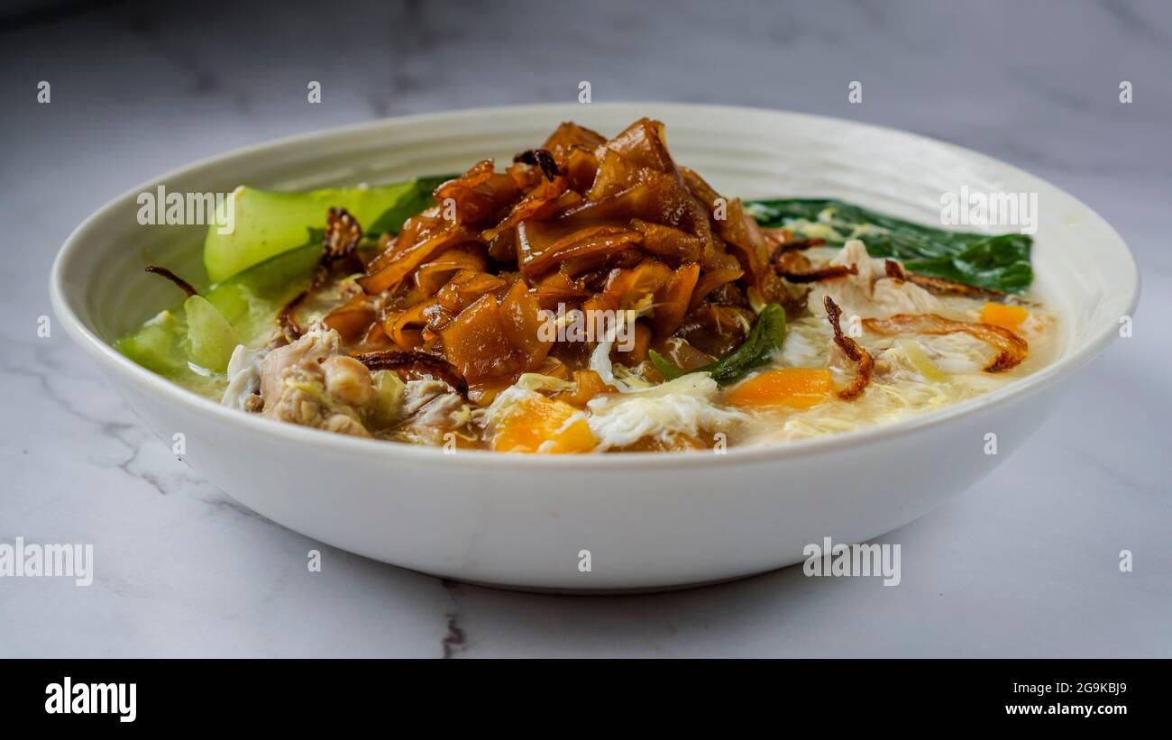 Flat Noodles cooked in Egg Gravy (Wan Tan Hor) with chicken bits and fish balls. Garnished with fried onions. A chinese cuisine served in Southeast As Stock Photo