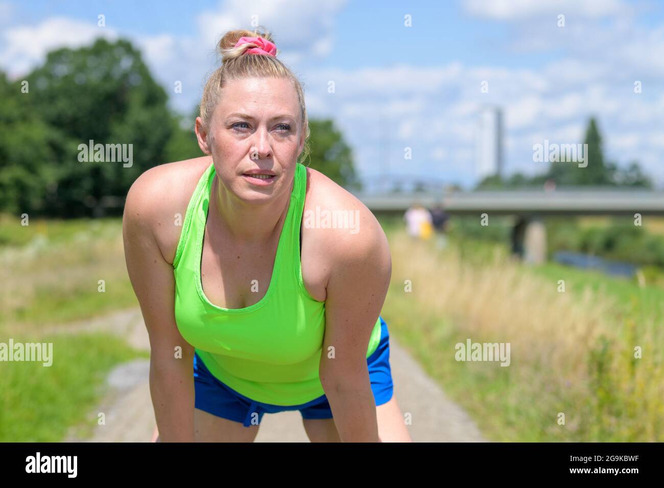 Middle-aged woman pausing while jogging to catch her breath leaning towards the camera and looking aside with a thoughtful expression in a healthy act Stock Photo