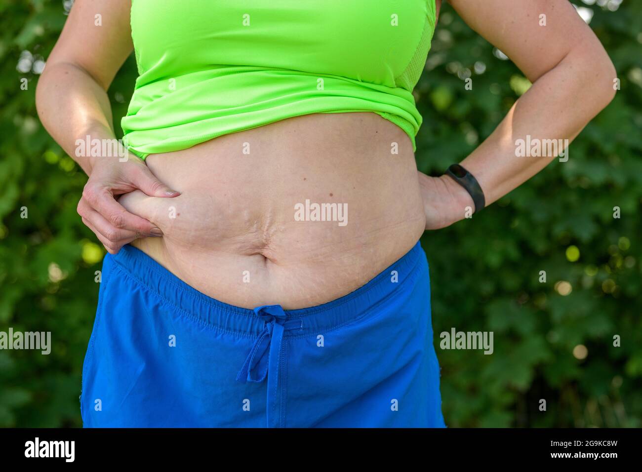 Overweight woman pinching the excess fat on her stomach between her fingers in a close up view of her midriff in sporting attire Stock Photo