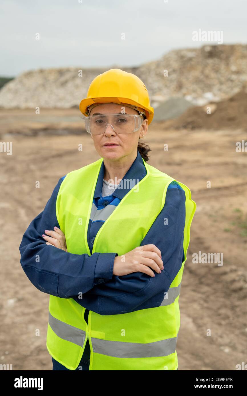 Female builder with crossed arms standing against quarry or construction site Stock Photo