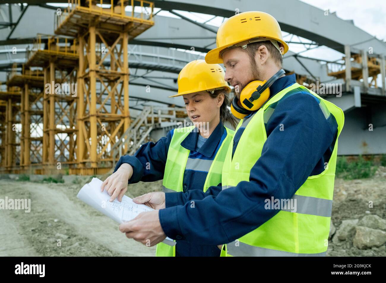 Two workers in work helmets examining blueprint during their work on construction site Stock Photo