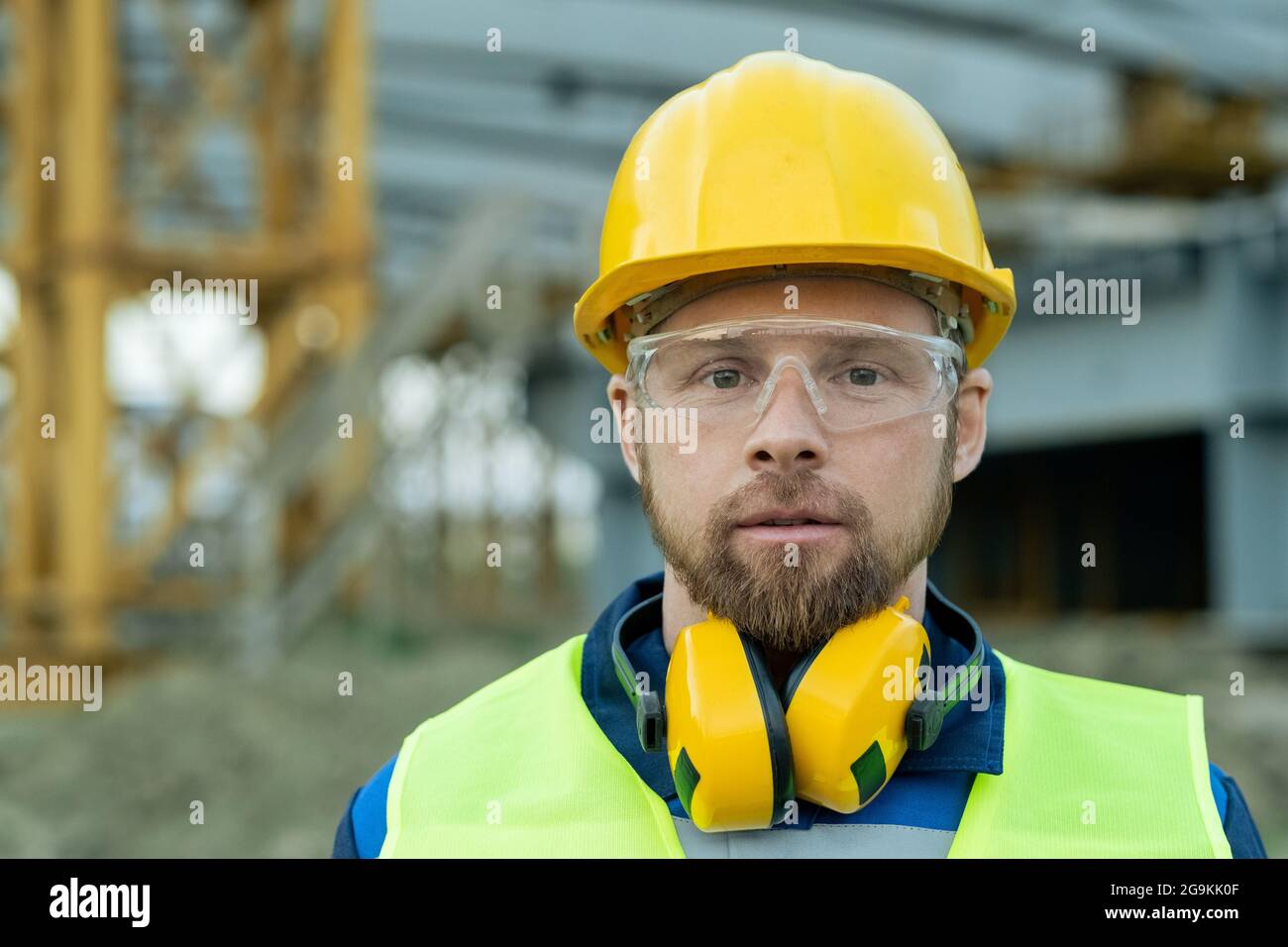 Close-up of construction worker in work helmet and in headphones looking at camera standing outdoors Stock Photo