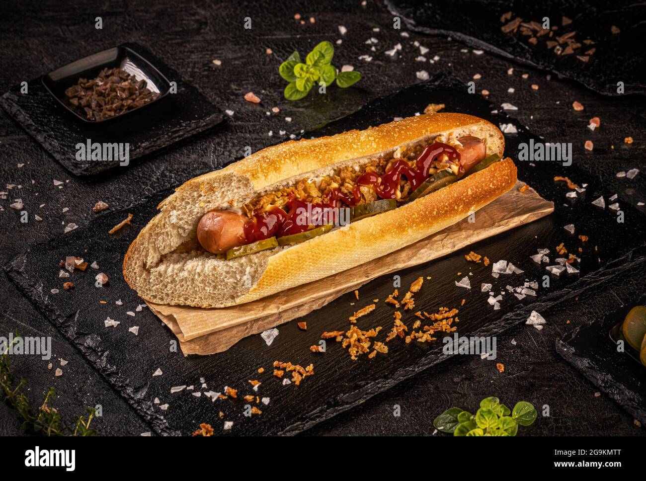 Delicious hot dog with pickles, dried onion and ketchup on black slate
