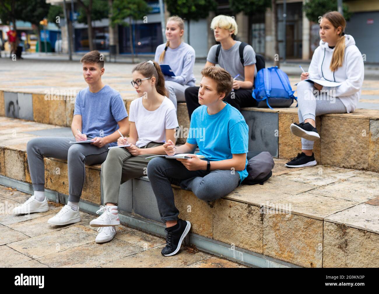 Teen students sitting with workbooks in schoolyard Stock Photo