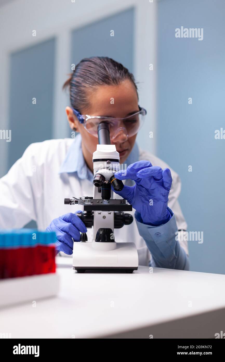 Microbiologist woman looking into medical microscope analyzing virus ...