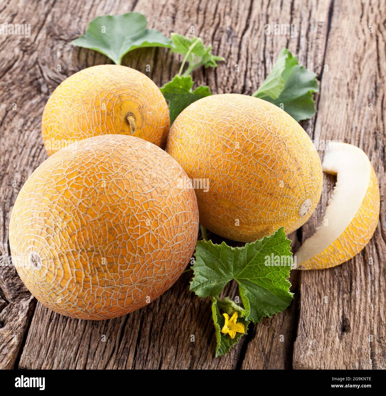 Ripe yellow melon with slices and melon leaves on a old wooden table. Stock Photo