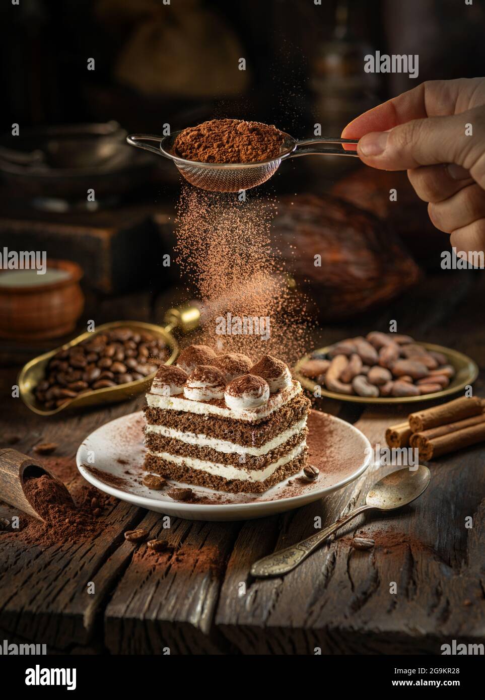 Dusting Tiramisu Like Cake With Cocoa Powder Still Life With Slice Of Cake And Coffee And Cacao Beans On Wooden Table Stock Photo Alamy