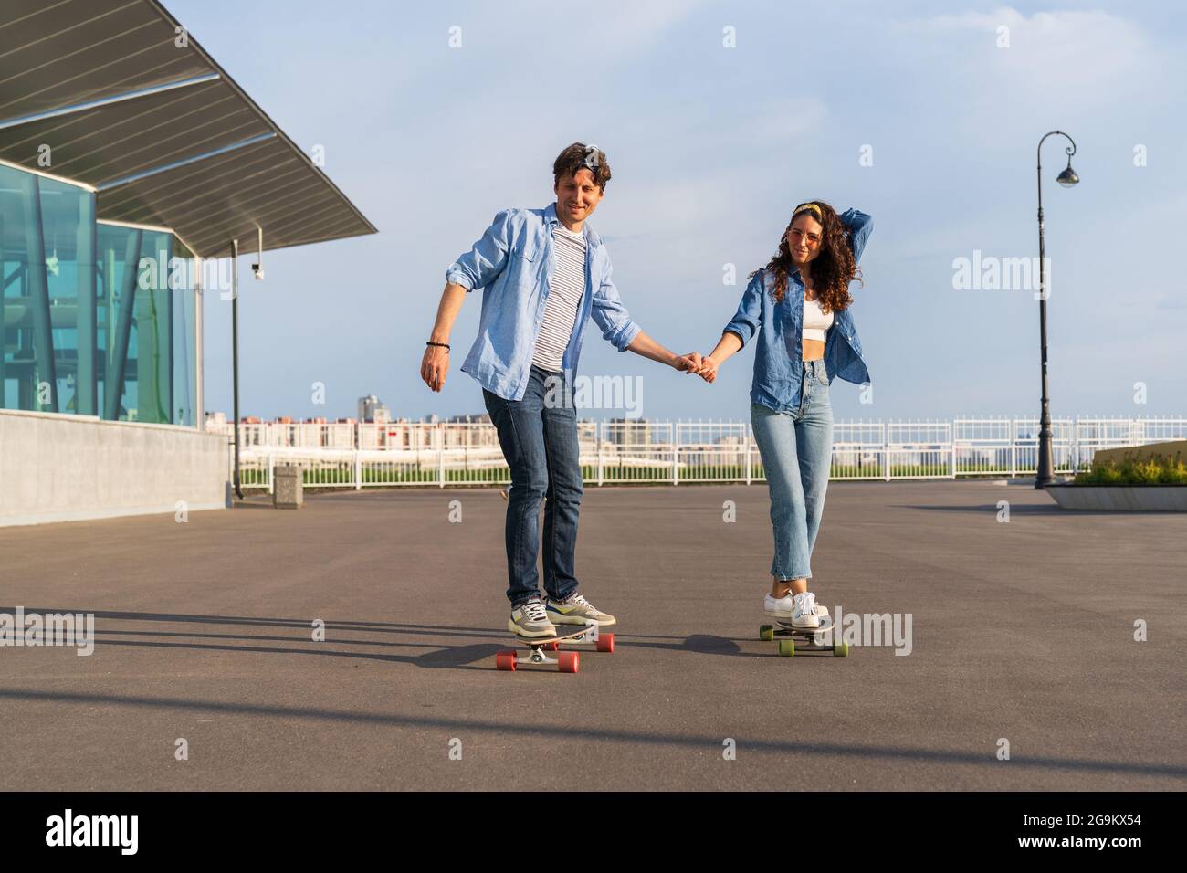 Young adult riding longboard on summer city street. Hipsters couple on skateboards in urban area Stock Photo