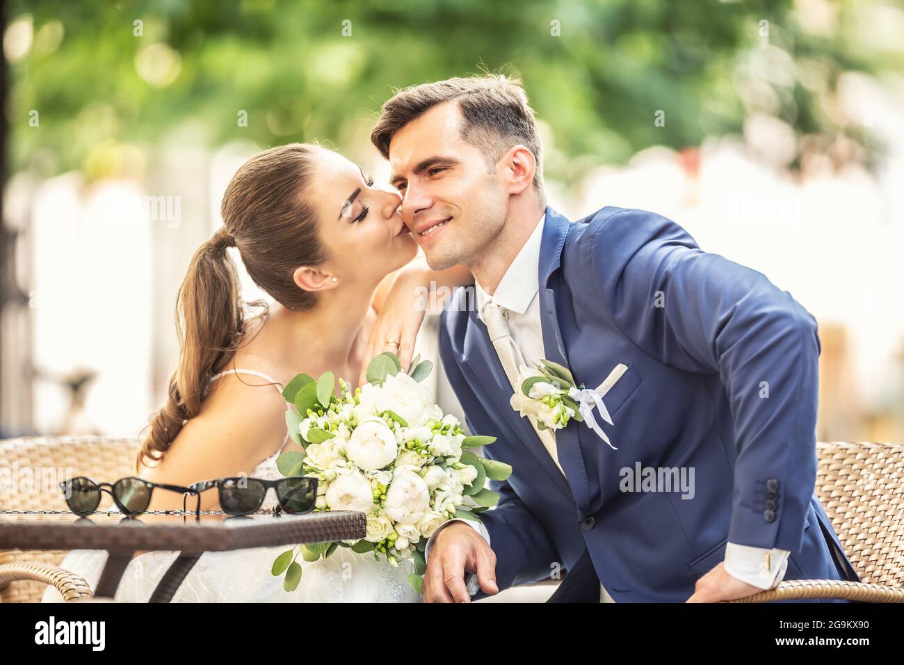 Loving bride kissing her charming huband. They wear wedding robes and hold  beautiful bouquet Stock Photo - Alamy