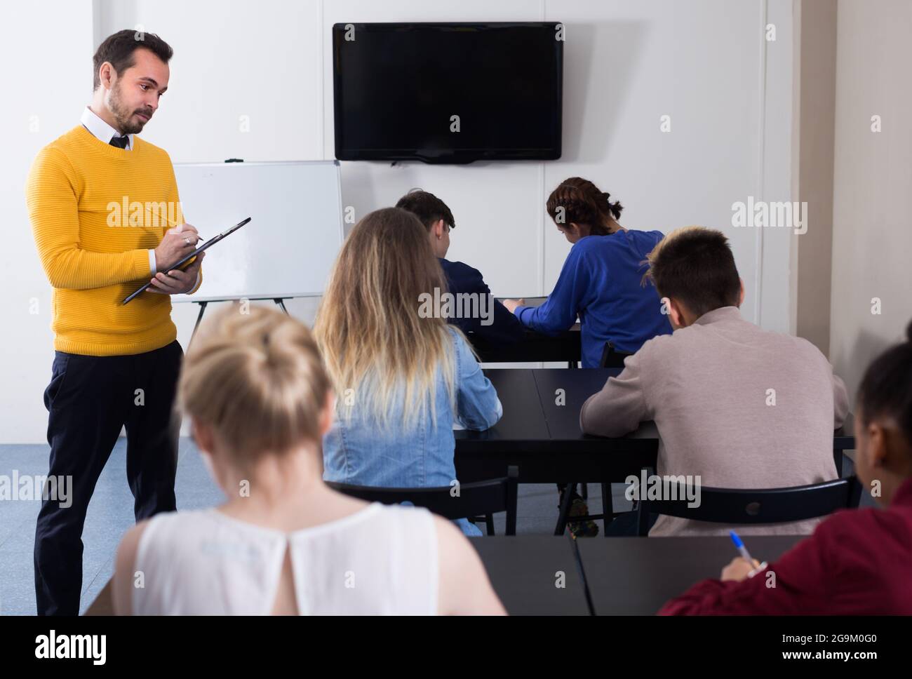 University teacher is monitoring students during revision work in class. Stock Photo