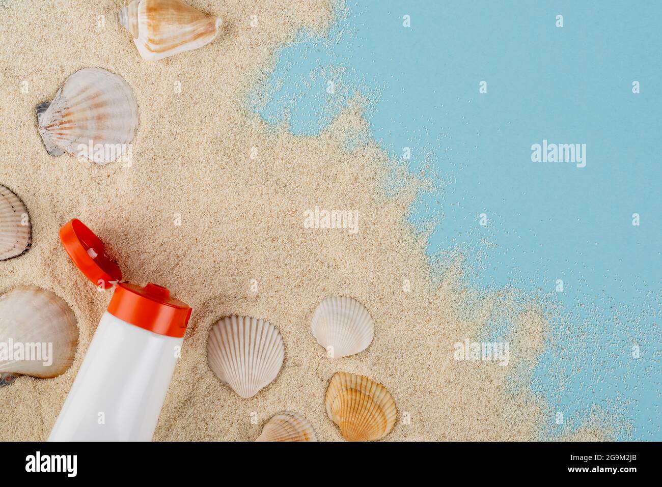 top view of tube of sunblock and seashells on sand and blue surface Stock Photo