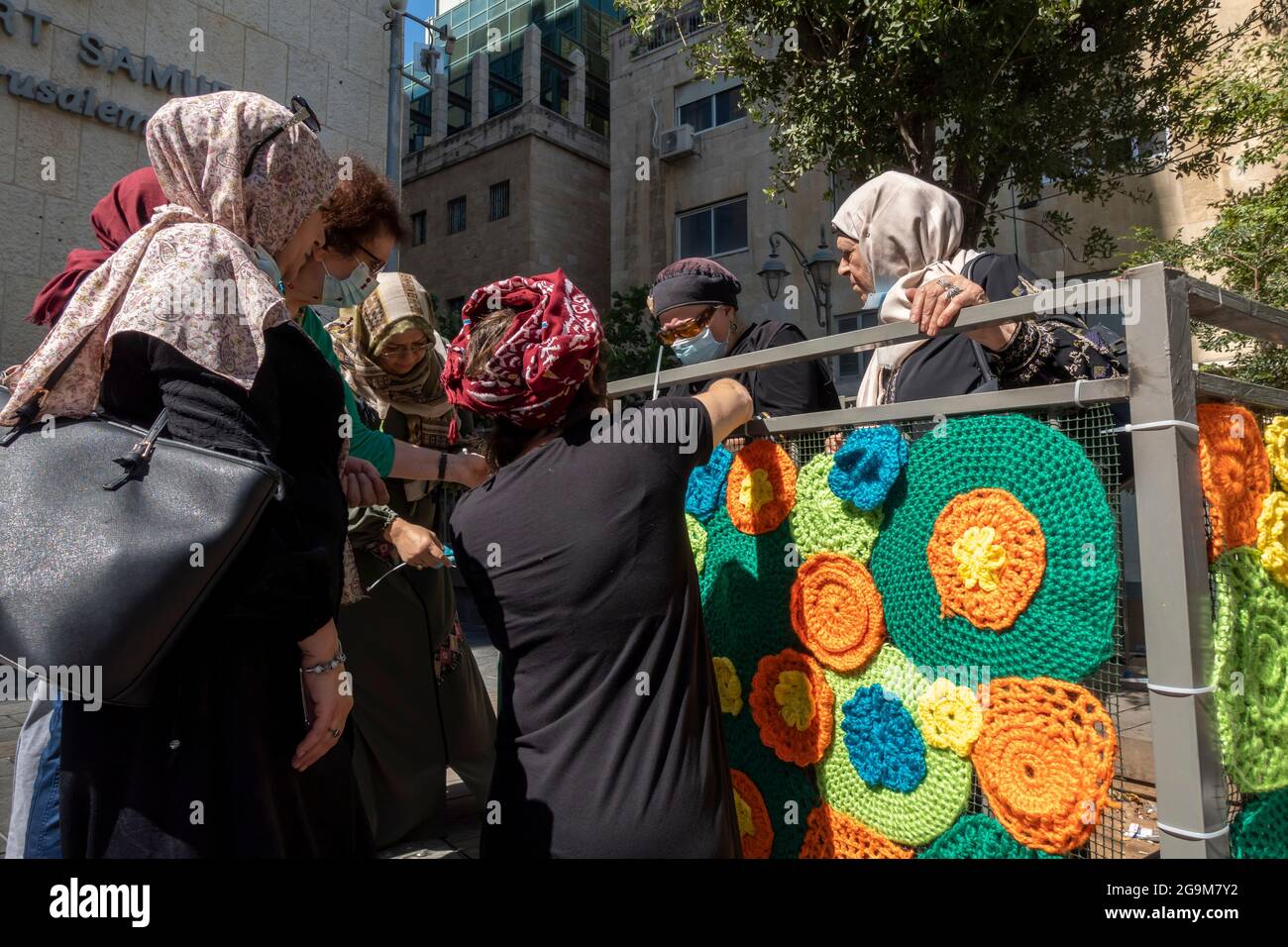 Israeli Jewish and Arab women wrap a fence with colourful knitted and
