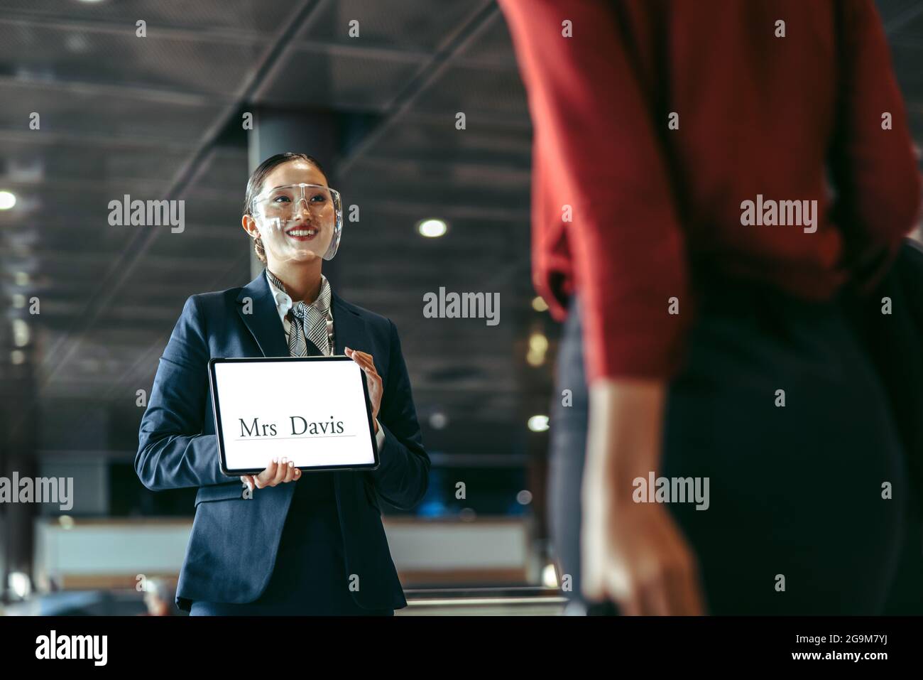 Private driver wearing face shield standing at airport terminal holding