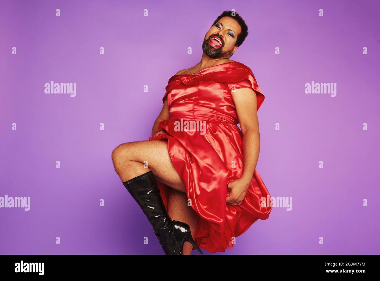 Full length of gay man wearing women clothing dancing and performing in studio. Androgynous male wearing red shiny dress. Stock Photo