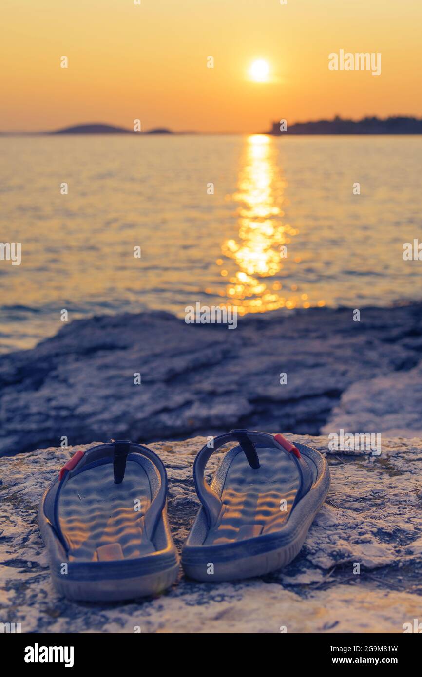 Flip-flops, sandals on beach and setting sun in background. Travel, summer vacations, tourism and relaxation concepts Stock Photo